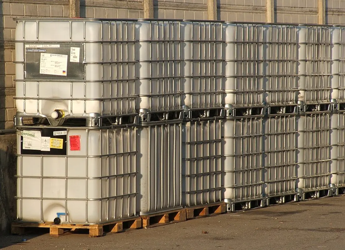Rangées de cuves IBC blanches dans leurs cages acier galvanisé, sur palettes bois, dans un dépôt industriel